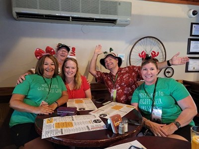 People dressed in Christmas shirts sit at a table and smile at the camera. Photo