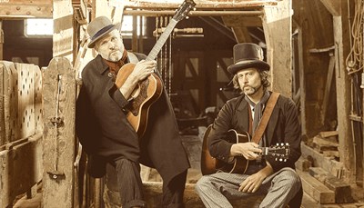 David Berkeley and Ben Parker holding instruments, sitting in a barn. Photo