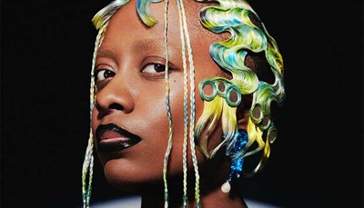 Portrait of Cécile McLorin Salvant with blue and yellow hair, with a black background. Photo