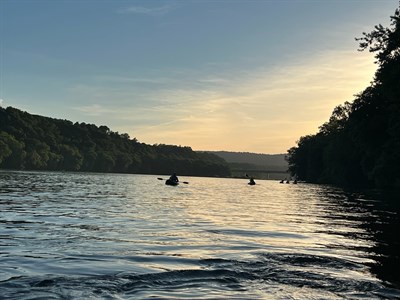 People on the river in kayaks with the sunset in the background.  Photo