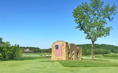 Picture of a fairway that has a stone wall with an American flag hanging along the side. Photo
