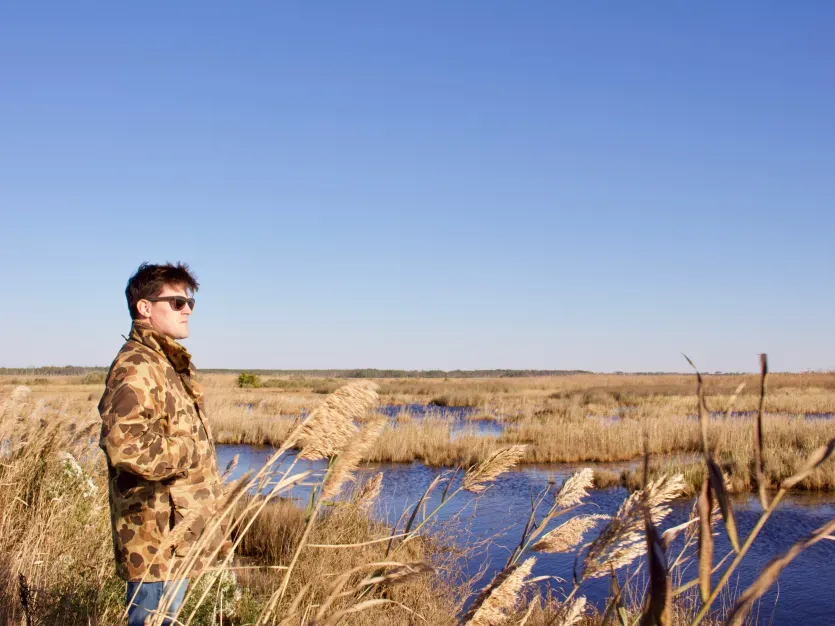 Man in camouflage jackets overlooks a marsh