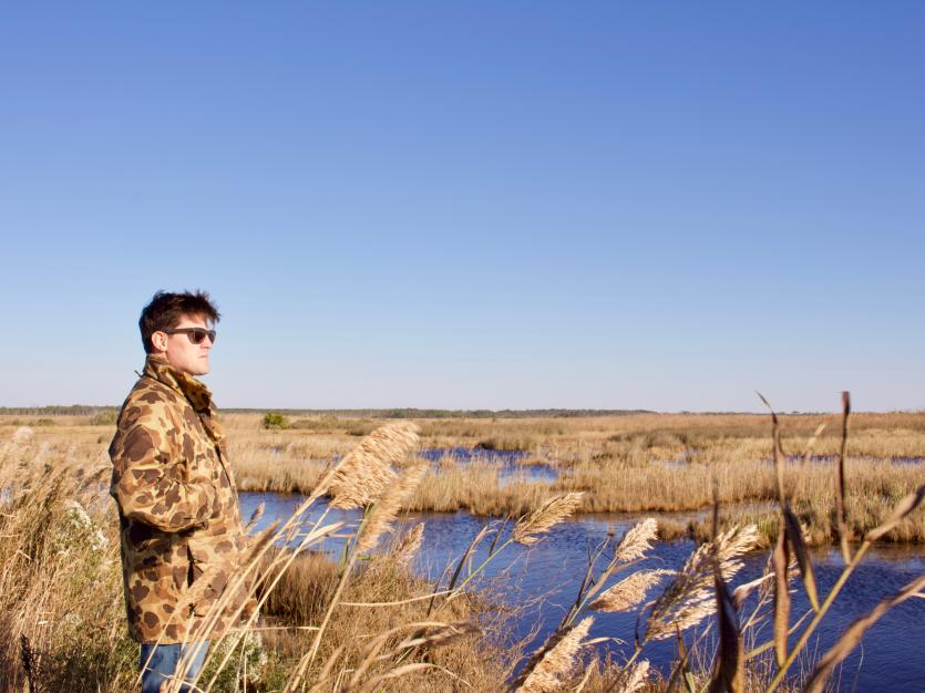 Man in camouflage jackets overlooks a marsh