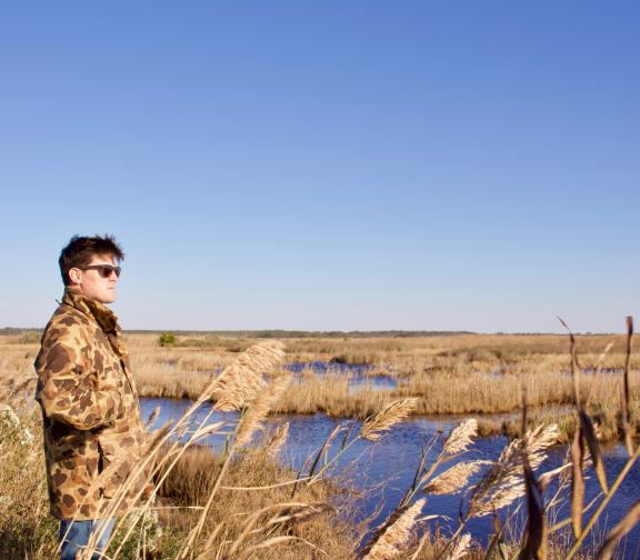 Man in camouflage jackets overlooks a marsh