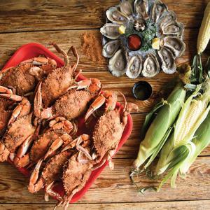 A tray of steamed crabs with a platter of steamed oysters on the half-shell and a few ears of corn.