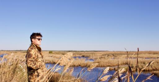 Man in camouflage jackets overlooks a marsh