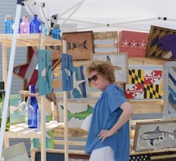 A woman looks at artwork in an outdoor booth. Photo