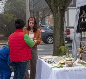 A woman talks with another woman about jewelry for sale at an outdoor booth. Photo