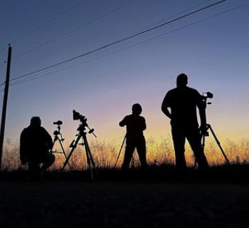 A group of amateur astronomers look at the night sky in profile.  Photo