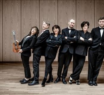 Ukulele Orchestra of Great Britain wearing tuxedos and leaning against each other. Photo