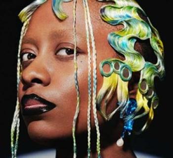 Portrait of Cécile McLorin Salvant with blue and yellow hair, with a black background. Photo