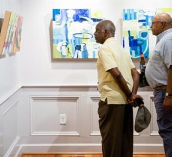 Photo of two men in Mansion gallery, gazing at artwork on wall. Photo