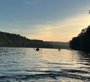 People on the river in kayaks with the sunset in the background. Photo