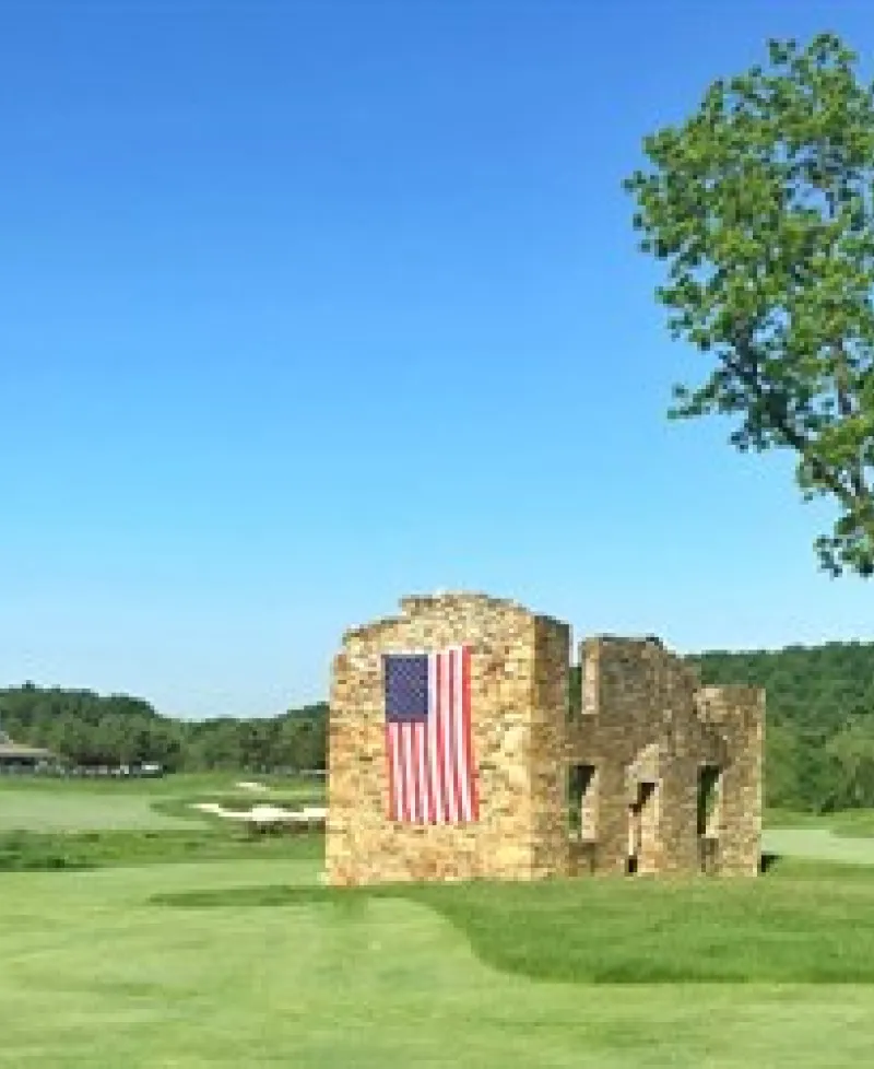 Picture of a fairway that has a stone wall with an American flag hanging along the side. Photo