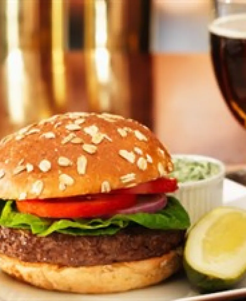 A tasty burger with tomato, lettuce and onion joined with a pickle, cole slaw and a cold beer. Photo