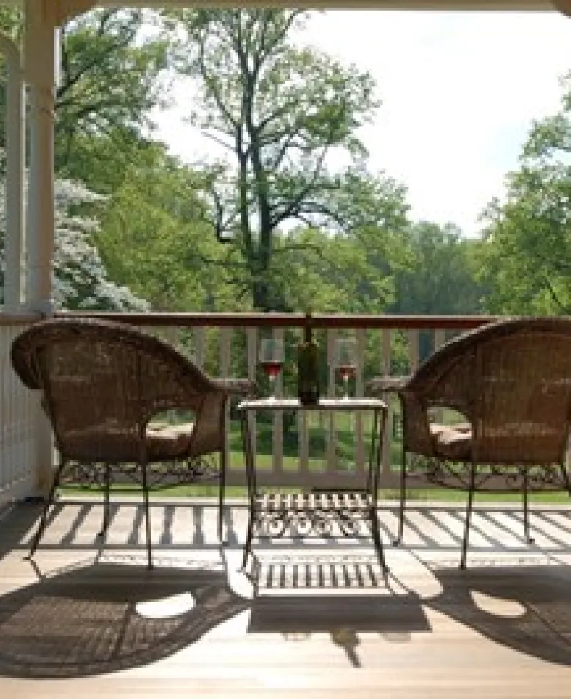 Two chairs and a table with a bottle of wine and two glasses on a porch at the Thanksgiving Farm. Photo