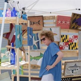A woman looks at artwork in an outdoor booth. Photo