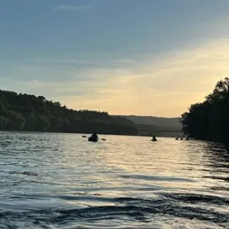 People on the river in kayaks with the sunset in the background.  Photo