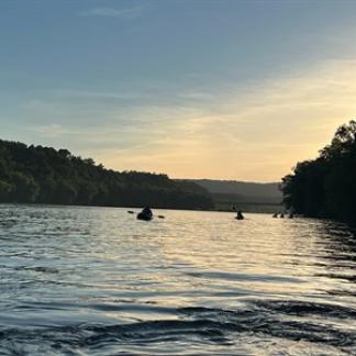 People on the river in kayaks with the sunset in the background.  Photo