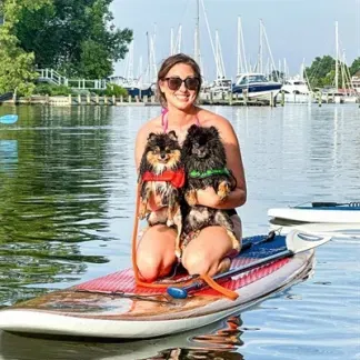 Person kneeling on a paddleboard and holding two dogs Photo
