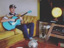 Wax sitting on a couch playing a guitar Photo